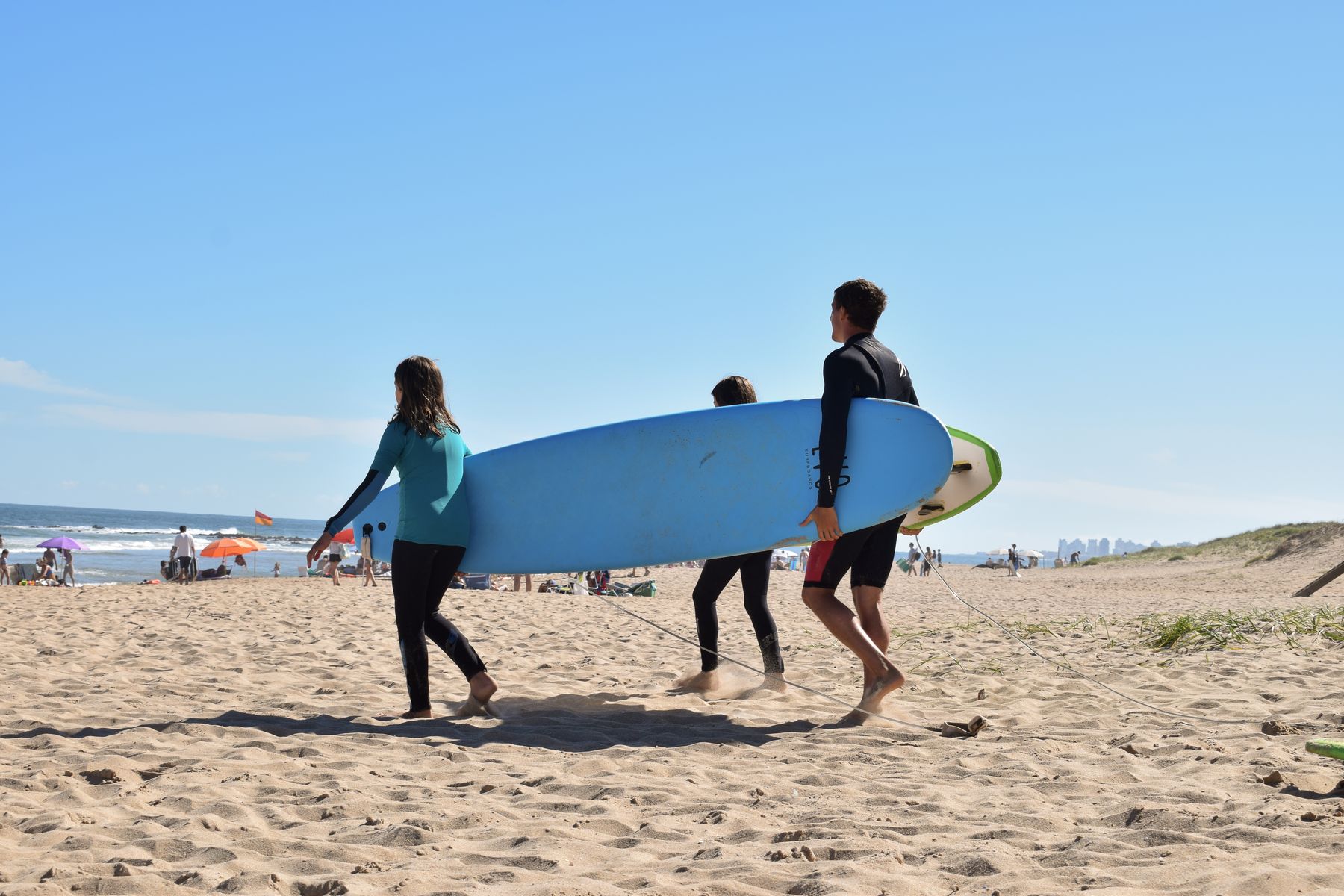 Instructor y alumnas de Las Toninas caminando con una tabla de surf en Playa Brava